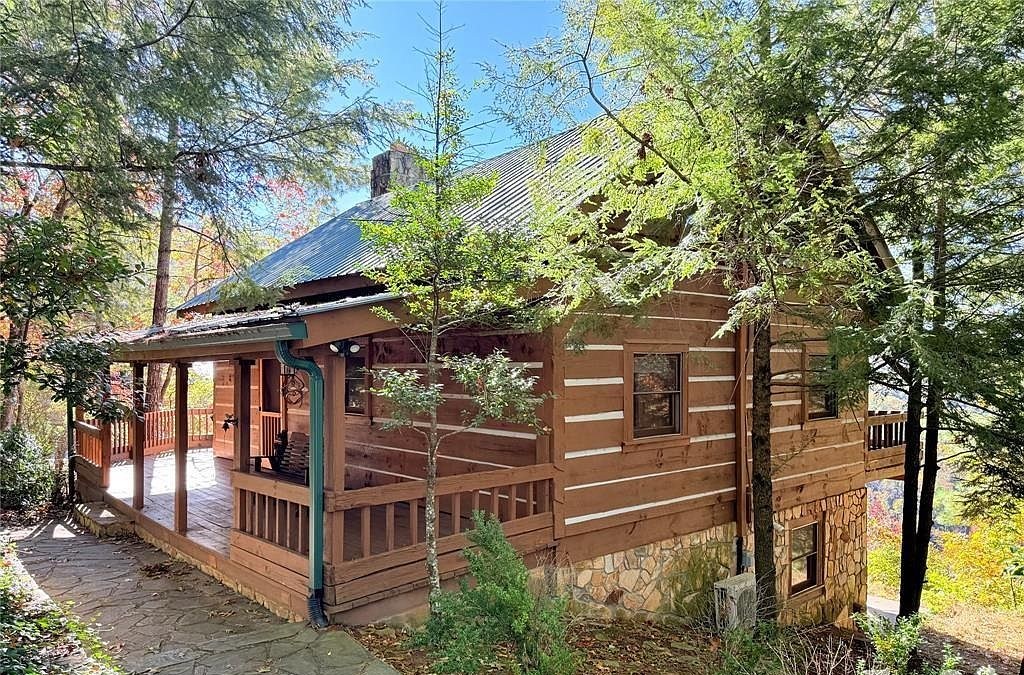 The log cabin from the flagstone walk, covered porch and metal roof under tall pines